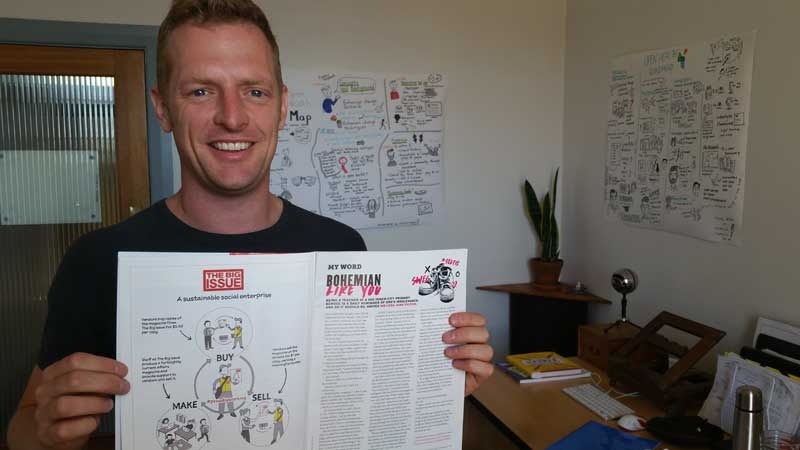 Matt holding up a copy of The Big Issue magazine, open to the page that has the diagram he sketched.