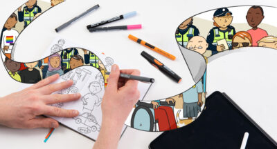Hand drawing comics in a sketchbook on a white table scattered with colored markers.