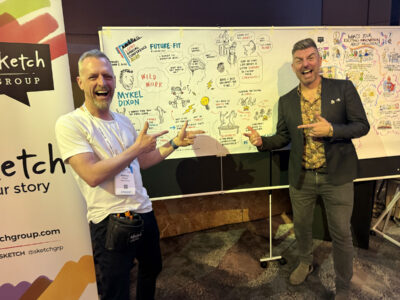 An image of 2 men pointing at the graphic recording canvas behind them.